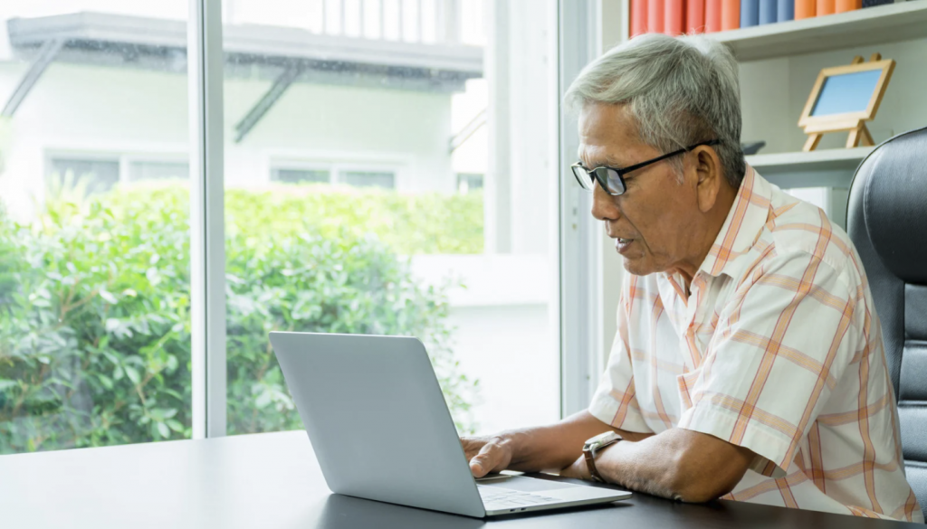 Older man sitting at desk completing cognitive screen on laptop