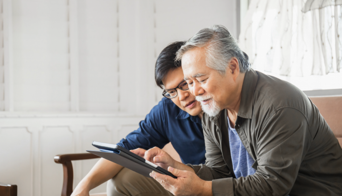 two Asian men seated on a couch looking at a tablet