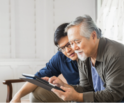 two Asian men seated on a couch looking at a tablet