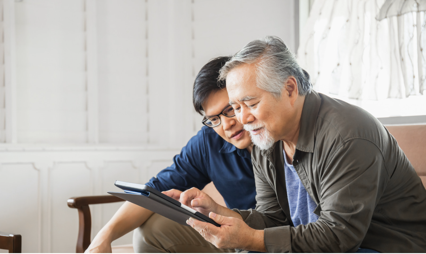 two Asian men seated on a couch looking at a tablet