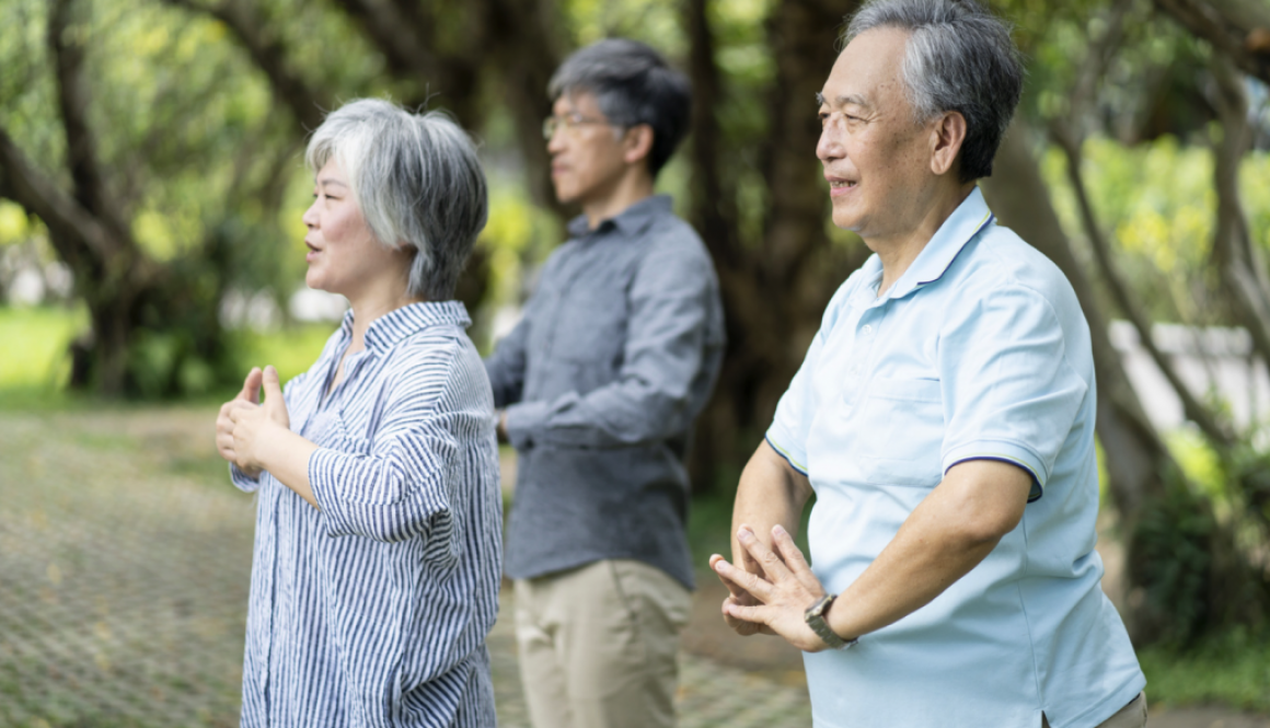 Three Asian adults practicing Tai Chi outdoors